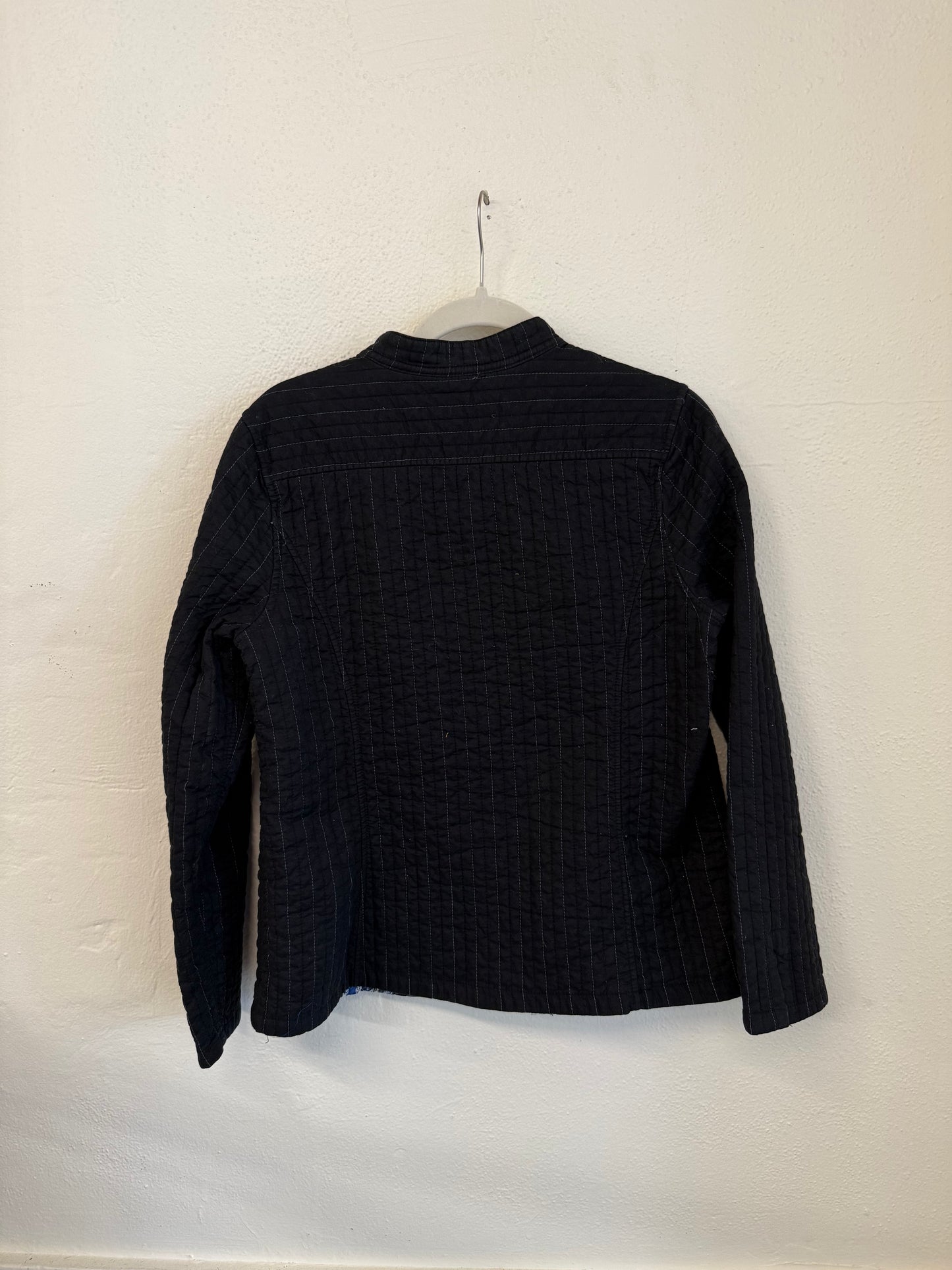 Black textured jacket on a hanger against a white wall