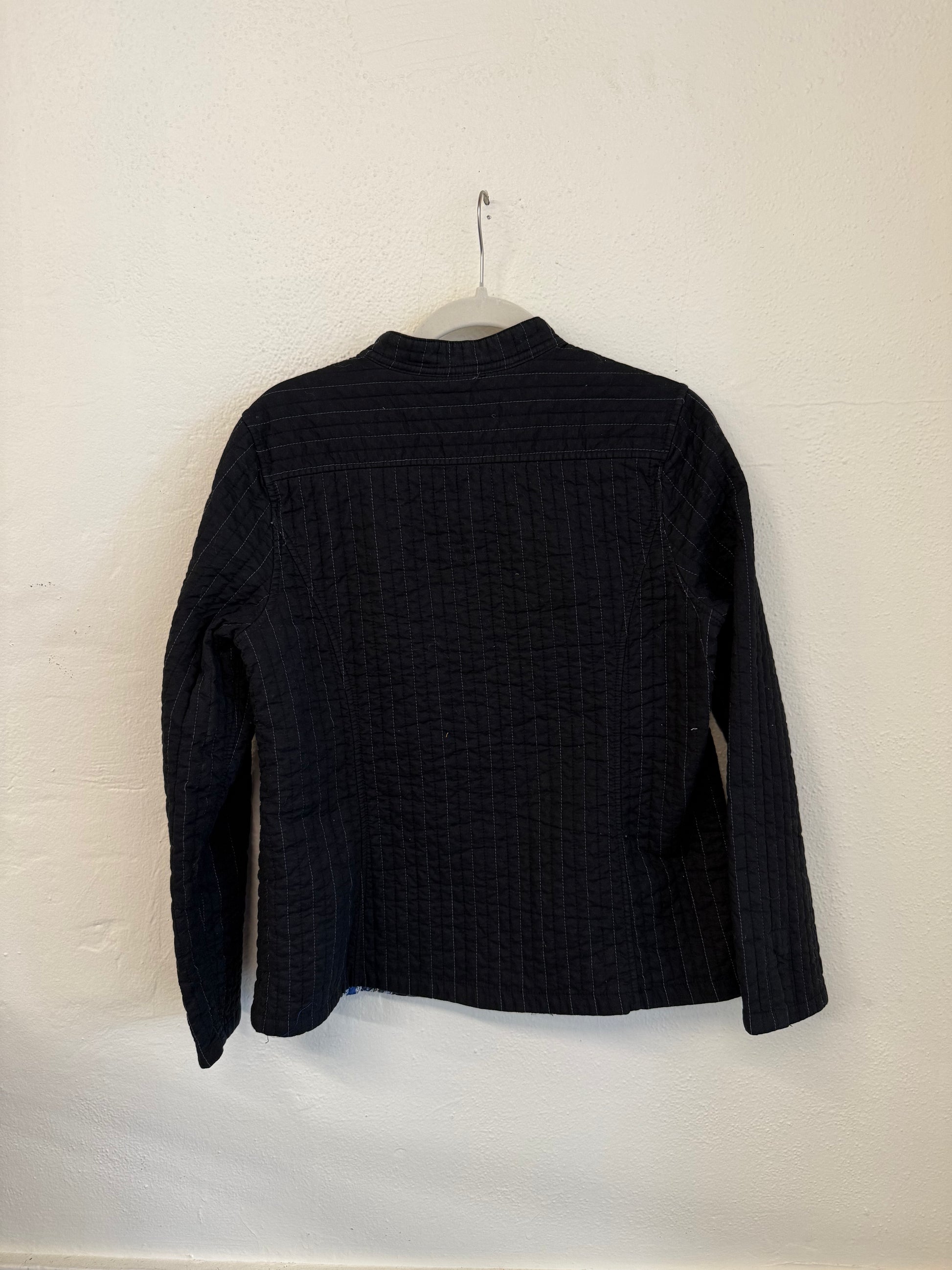 Black textured jacket on a hanger against a white wall